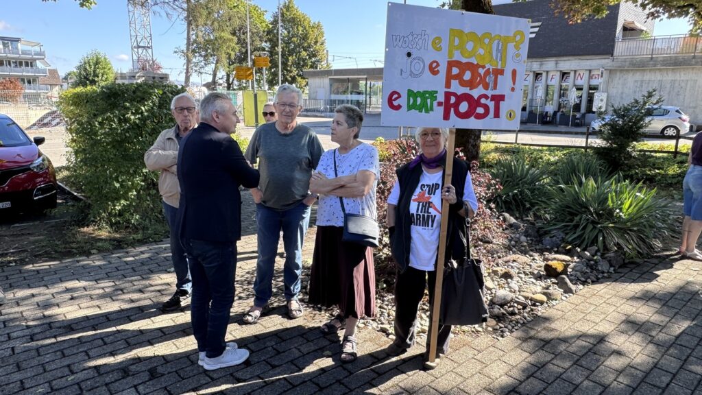 Frau mit selbstgemachtem Schild: wotsch e Poscht? Jo e Poscht! E Dorf-Post